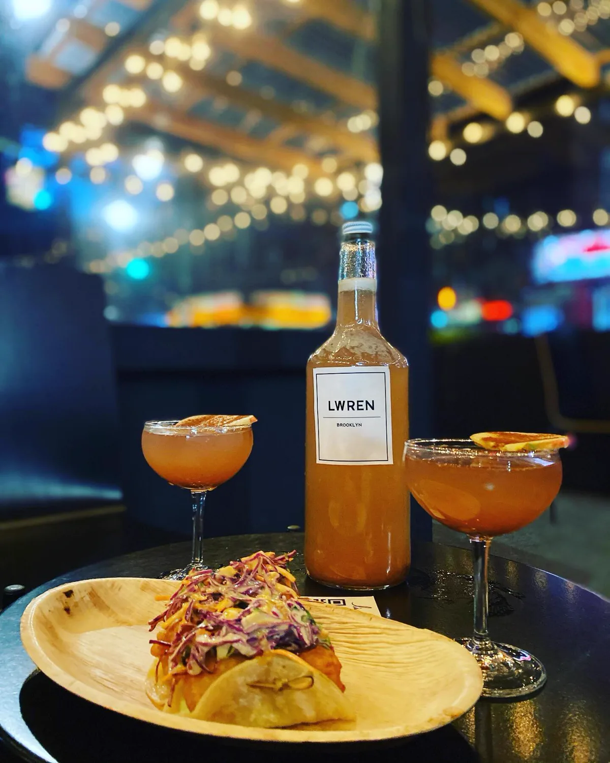 Two spritz cocktails and a bottle of L'Wren house wine under string lights
